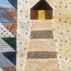 May include: A patchwork quilt featuring a lighthouse design. The lighthouse has a black roof and a brown body with a yellow accent. The tower is white with black and white striped sections. The quilt incorporates various patterned fabrics.