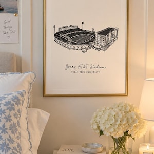 May include: A framed wall art print featuring a black and white line drawing of Jones AT&T Stadium at Texas Tech University. The print is centered in a thin gold frame and displays the stadium name and university in black text below the illustration.
