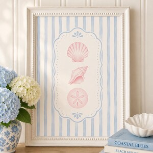 May include: A framed wall art print featuring a vertical arrangement of three pink seashells centered within a decorative scalloped border on a light blue and white striped background, housed in a white beaded frame with a classic rectangular shape.