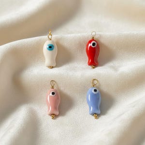 以下が含まれることがあります： 金色のアクセントが付いた、カラフルな魚の形をした4つのチャーム。チャームは白、赤、ピンク、青で、それぞれに目のディテールが1つあります。チャームは金色のループから吊り下げられています。
