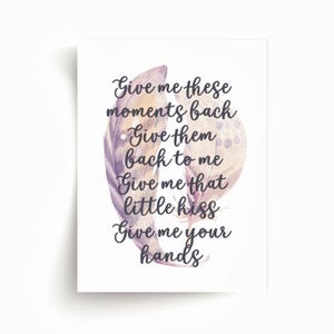 May include: A white print featuring watercolor feathers in shades of purple, tan, and brown. The print includes the text "Give me these moments back, Give them back to me, Give me that little kiss, Give me your hands."