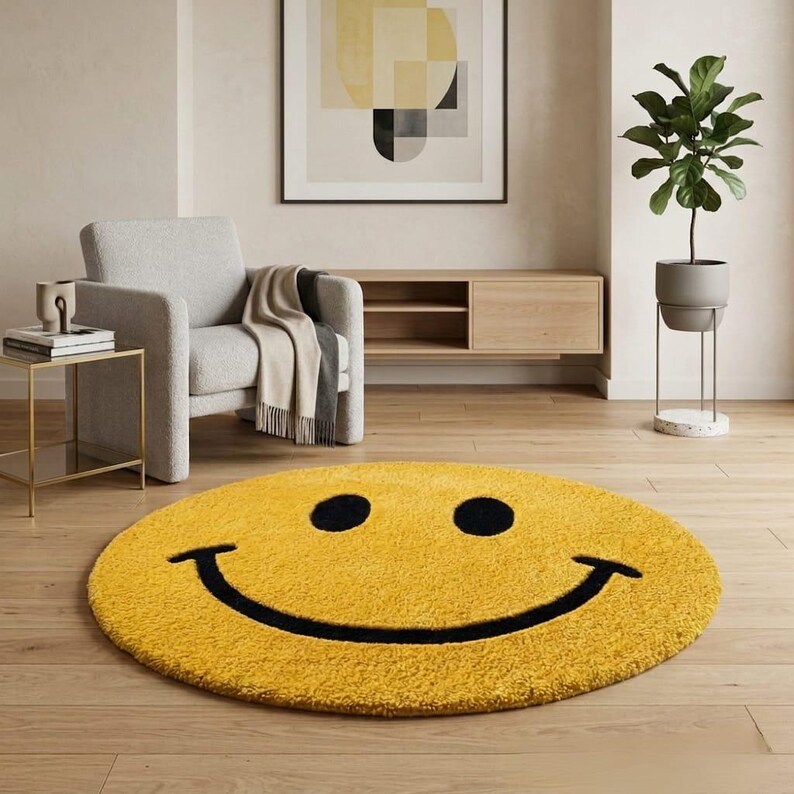 Pu&ograve; includere: Un tappeto rotondo giallo con un grande design a faccina sorridente nera. Il tappeto &egrave; posto su un pavimento in legno in una stanza con una poltrona grigia, un tavolino e una pianta in vaso. Il design del tappeto &egrave; semplice e audace.