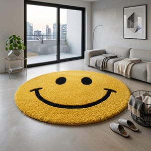 Pu&ograve; includere: Un tappeto rotondo giallo con un design a faccina sorridente. Il tappeto presenta occhi neri e una bocca nera curva. Il tappeto &egrave; posto su un pavimento di colore chiaro in un moderno soggiorno.