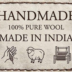 May include: A cream fabric label with the text "HANDMADE", "100% PURE WOOL", and "MADE IN INDIA" in dark brown. The label includes illustrations of a hand with yarn, a sheep, and a loom.