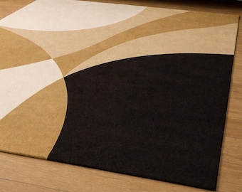 May include: A rectangular area rug with a modern design. The rug features a black, tan, and cream color palette with curved geometric shapes. The rug is placed on a hardwood floor, with a beige sofa visible in the background.