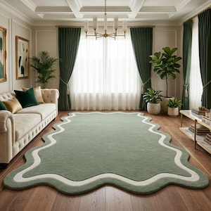 Op de afbeelding: Een woonkamer met een groot, saliegroen tapijt met een golvende, crèmekleurige rand. De kamer omvat een beige bank met groene en gouden kussens, groene gordijnen en ingelijste kunstwerken. De houten vloer voegt warmte toe aan de ruimte.