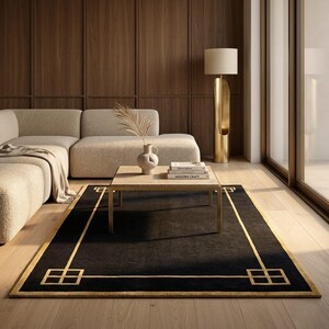 May include: A black rectangular rug with a gold geometric border and accents. The rug is placed in a living room setting with a beige sectional sofa, a wooden coffee table, and a gold floor lamp.