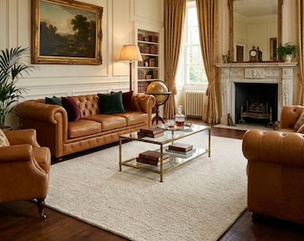May include: A luxurious living room featuring a brown leather Chesterfield sofa and matching armchairs. A glass-top coffee table sits on a cream-colored rug. The room includes a fireplace, a large mirror, and a landscape painting.