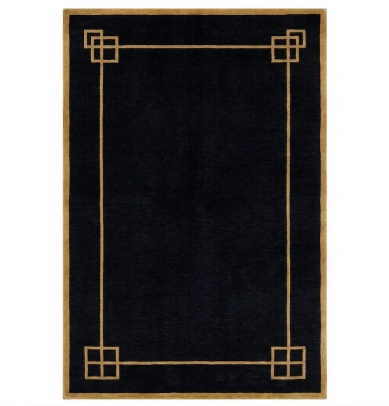 May include: A rectangular black rug with a gold border and geometric corner designs. The rug's dark colour and simple design create a modern aesthetic. The rug is suitable for living rooms, bedrooms, or entryways.
