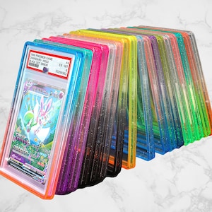 May include: A collection of graded Pokémon trading cards in clear, colorful protective cases. The cases are arranged in a row, showcasing a variety of vibrant colors including pink, blue, green, and yellow. One card is visible, featuring a Sylveon character.