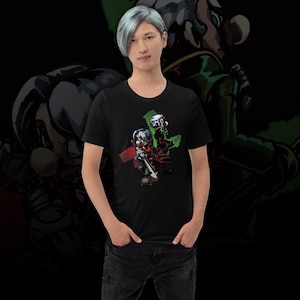 May include: Black t-shirt with a cartoon illustration of two anime characters. One character holds a sword, and the other stands with a green backdrop. The background is black.