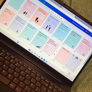 Peut inclure: Un ordinateur portable noir affichant un document intitulé "Move and Thrive - Parent guide". L'écran montre des pages colorées avec du texte et des illustrations. L'ordinateur portable est ouvert sur une surface verte à motifs.