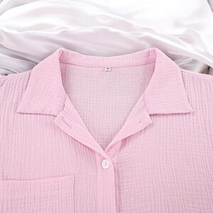 Puede incluir: Una camisa abotonada de color rosa claro con un acabado de tela texturizada y arrugada, cuello cl&aacute;sico y un bolsillo frontal. La etiqueta interior del cuello muestra la talla M. La prenda est&aacute; confeccionada con un cierre de botones visible.