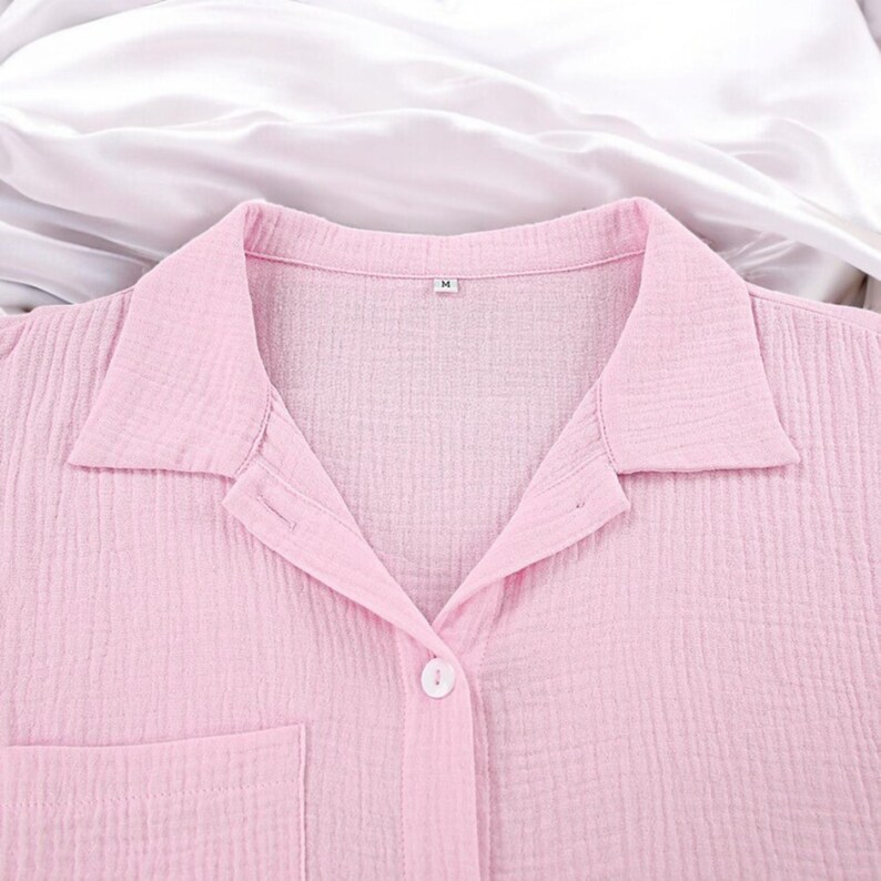 Puede incluir: Una camisa abotonada de color rosa claro con un acabado de tela texturizada y arrugada, cuello cl&aacute;sico y un bolsillo frontal. La etiqueta interior del cuello muestra la talla M. La prenda est&aacute; confeccionada con un cierre de botones visible.