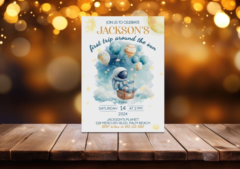 May include: A white invitation card with a blue watercolor background featuring an astronaut in a hot air balloon with planets and stars. The text reads "JOIN US TO CELEBRATE JACKSON'S first trip around the sun MAY 14 AT 2PM 2024 JACKSON'S PLANET 129 MERCURY BLVD, PALM BEACH RSVP to Give at 842-123-4567"