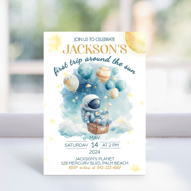 May include: A blue and white astronaut-themed first birthday party invitation with a watercolor background. The invitation features a cartoon astronaut holding a star in a basket attached to balloons. The text reads "Join us to celebrate Jackson's first trip around the sun" and includes the date, time, and location of the party.