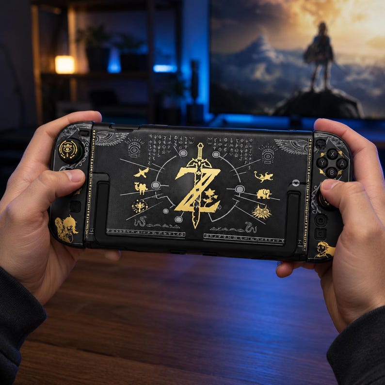 May include: A black handheld gaming console featuring gold-colored graphics, including a central sword and letter Z emblem, surrounded by various small icons and ancient-style script. The controllers have matching gold accents and character silhouettes.