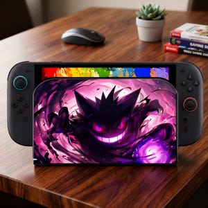 Può includere: Console Nintendo Switch nera con una skin personalizzata con un design Gengar viola e nero. La console è su un tavolo di legno, con un mouse, una piccola pianta e custodie di gioco sullo sfondo.