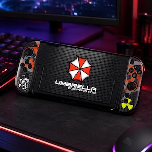 May include: A handheld gaming console featuring a black textured skin with the Umbrella Corporation logo and text in white and red. The sides display orange and grey splatter patterns, a gas mask graphic, and a yellow radioactive hazard symbol.