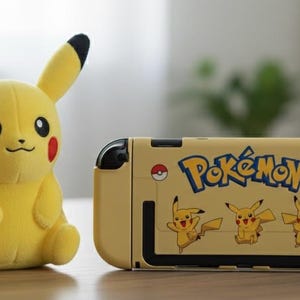 Peut inclure: Un jouet en peluche Pikachu jaune est à côté d'une console Nintendo Switch jaune. La console affiche le logo "Pokémon" et des graphiques Pikachu. La peluche a des oreilles à bout noir et des joues rouges.