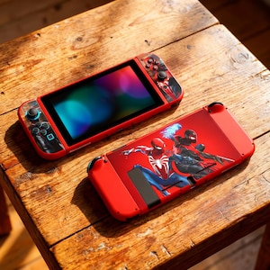 Può includere: Console Nintendo Switch rossa a tema Spider-Man. La console presenta uno schermo vibrante e un case rosso con grafica di Spider-Man. I controller Joy-Con hanno un design nero e rosso. La console è su una superficie di legno.