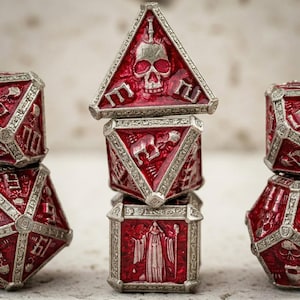 Könnte beinhalten: Ein Satz roter und silberner polyedrischer Würfel mit detaillierten Gravuren. Die Würfel zeigen Schädel-, Figuren- und geometrische Designs. Die Würfel sind gestapelt und angeordnet, um ihre komplizierten Details zu präsentieren, ideal für Tabletop-Spiele.