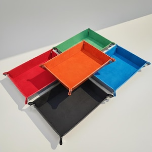 May include: A collection of five rectangular valet trays in vibrant colours including red, orange, green, blue, and black. Each tray features raised sides with metal snap fasteners at the corners, creating a structured, open-top storage container.