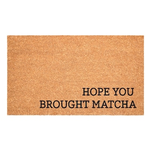 May include: A rectangular doormat with a light brown, textured surface. The black text reads "HOPE YOU BROUGHT MATCHA". This welcome mat is designed for a home's entryway.
