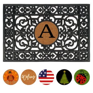 May include: Black rectangular doormat with an ornate scrollwork design. A circular insert in the center features the letter "A" on a brown background. Includes interchangeable seasonal inserts with a turkey, "Welcome" text, American flag, Christmas tree, and ladybug.
