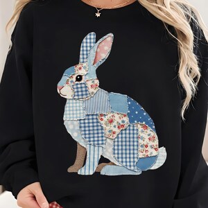 Pode incluir: Camisola preta com um design de coelho em patchwork em tons de azul, branco e padrões florais vermelhos. O coelho está sentado, com as orelhas levantadas. Um estilo casual e confortável.