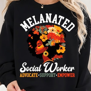 May include: Black sweatshirt with the word "MELANATED" above a graphic of a woman's profile with floral hair. The words "Social Worker" and "ADVOCATE • SUPPORT • EMPOWER" are below the graphic.