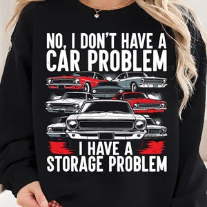 May include: Black sweatshirt with the text "NO, I DON'T HAVE A CAR PROBLEM I HAVE A STORAGE PROBLEM" above a graphic of classic cars in red, white, and gray. The cars are arranged in rows, with the text in white block letters.