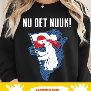 以下が含まれることがあります： 「NU DET NUUK！」の文字がプリントされた黒いスウェットシャツ。グリーンランドの国旗を持ったホッキョクグマのグラフィックが描かれています。クマはグリーンランドの青い輪郭の上に立っています。「PNG」、「INSTANT DOWNLOAD」、「SVG」の文字が下に表示されています。