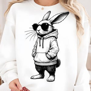 May include: White sweatshirt featuring a black and white illustration of a rabbit wearing sunglasses and a hoodie. The rabbit is standing with its hands in its pockets, giving a cool vibe. The design is a fun, graphic style.