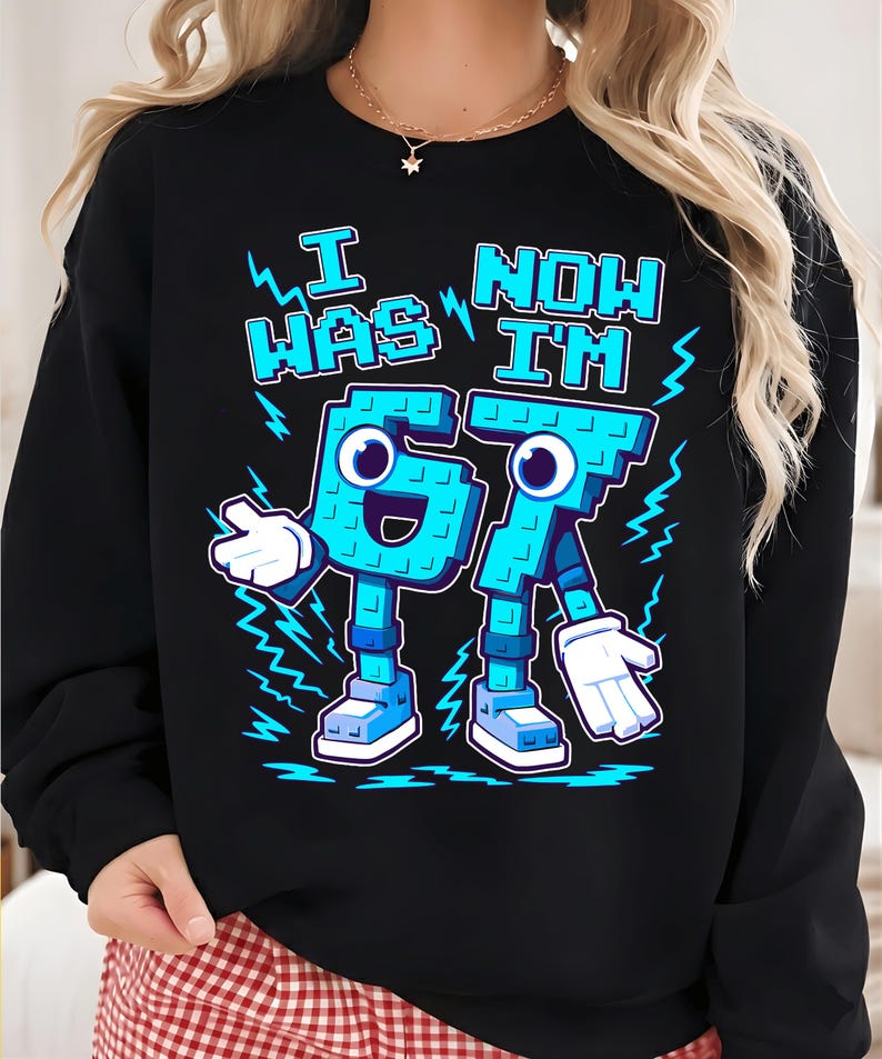 May include: Black sweatshirt with the text "I WAS 67 NOW I'M 67" in light blue. The numbers are designed as cartoon characters with arms, legs, and faces. The design includes lightning bolt accents.