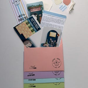 May include: A collection of stationery items including a September calendar card, a newsletter, a striped bookmark, and five colourful envelopes in pink, purple, blue, green, and orange. Each envelope features a stamp with the text Little Steps Mail Club.