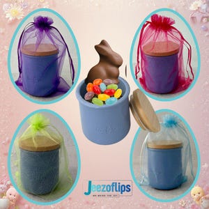 May include: An assortment of small, blue ceramic jars with wooden lids, some wrapped in sheer fabric bags. One jar contains a chocolate bunny and colorful jelly beans. The jars have the text "la ferme" on them.