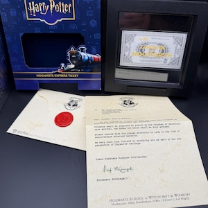 May include: A Harry Potter collectible set featuring a blue Hogwarts Express ticket box, a framed silver-toned ticket, and a cream-colored acceptance letter with a red wax seal. The letter includes the text Hogwarts School of Witchcraft & Wizardry.