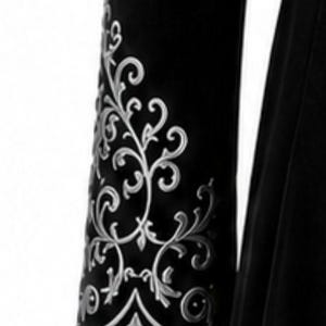May include: Close-up of a black garment sleeve with detailed silver floral embroidery. The design features swirling vines and leaves, creating a decorative pattern. The sleeve is made of a dark, possibly velvet, material.