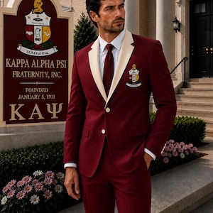 Pode incluir: Um paletó de terno vermelho escuro com lapelas cor de creme, uma gravata vermelho escuro combinando e uma camisa social branca. O paletó apresenta o brasão da fraternidade Kappa Alpha Psi, Inc. no peito. O terno inclui calças vermelho escuro.
