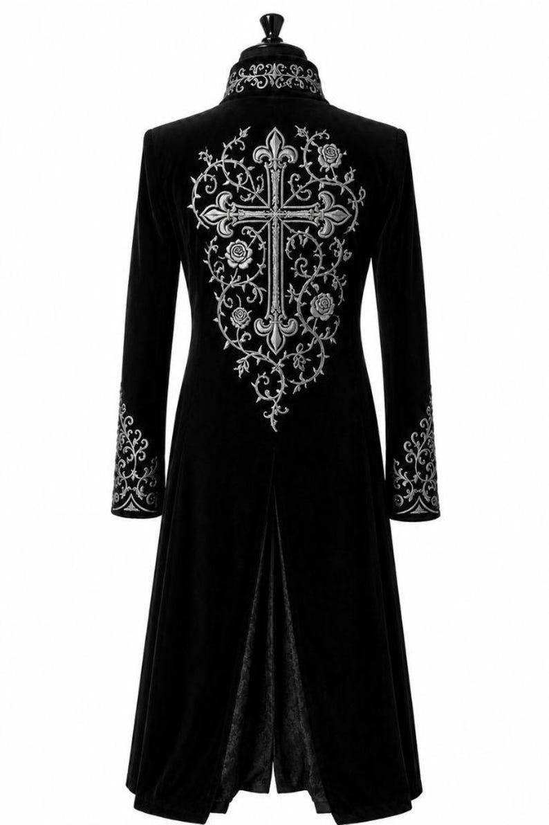 May include: A long black velvet coat with detailed silver embroidery. The back showcases a large cross design with floral and vine patterns. Silver embroidered accents adorn the sleeves and collar. A gothic-style garment.
