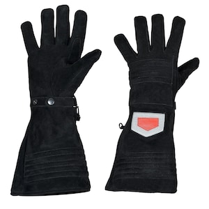 May include: A pair of black suede gloves with long cuffs. The gloves have a button closure at the wrist and a decorative patch with a red accent on the back of the hand. The gloves are designed with stitched details.