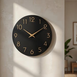 Pode incluir: Um relógio de parede redondo preto com algarismos e ponteiros dourados. O relógio está montado numa parede de cor clara. O design é minimalista e moderno, adequado para decoração de interiores.