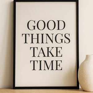 Könnte beinhalten: Gerahmter Druck mit den Worten "GOOD THINGS TAKE TIME" in fetten schwarzen Buchstaben auf cremefarbenem Hintergrund. Der Rahmen ist schwarz. Rechts vom Druck steht eine dekorative Vase auf einer Holzoberfläche.