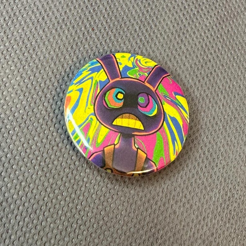 May include: A circular badge featuring a cartoon rabbit character. The rabbit is depicted in purple with a yellow mouth and a concerned expression. The background has a swirling pattern of vibrant colours including yellow, pink, blue, and green.