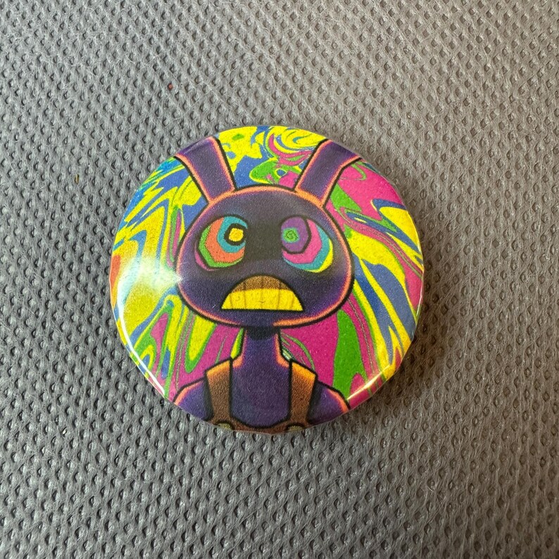 May include: A circular badge featuring a cartoon rabbit character. The rabbit is depicted in purple with a yellow mouth and a concerned expression. The background has a swirling pattern of yellow, pink, blue, and green.