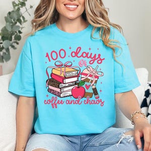 May include: A light blue t-shirt with a graphic design featuring the text "100 days of coffee and chaos." The design includes stacked books, a coffee cup, and an apple.