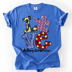 May include: A blue t-shirt with the word "LOVE" in a colorful design. The "L" is yellow with blue polka dots, the "V" is blue with red stripes, and the "E" is red with yellow polka dots. A puzzle piece with red hearts is in the center. The words "Autism Awareness" are below.