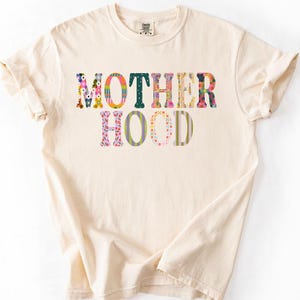 May include: A white ceramic mug with a black handle and the text "But First, Coffee" in a bold, black font. The mug is set against a blurred background, suggesting a cozy setting.