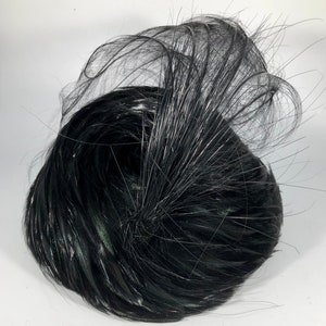 May include: A black feather hat with a large, curled feather on top. The hat is made of soft, fluffy feathers and has a round shape.